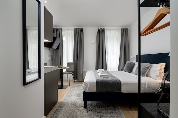Quarto de hotel moderno com uma cama, escrivaninha, cadeira e um espelho grande.
