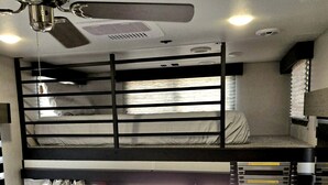 A bunk bed room with a ceiling fan, a window with curtains, and a view of the outside.