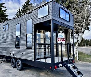 A modern RV with a covered front area, large windows, and a ramp for access. - Modern Lofted Tiny House Fully Equipped with Lake Views in Texas (Quitman)