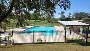 A fenced backyard with a swimming pool, a covered seating area, and a grassy lawn.