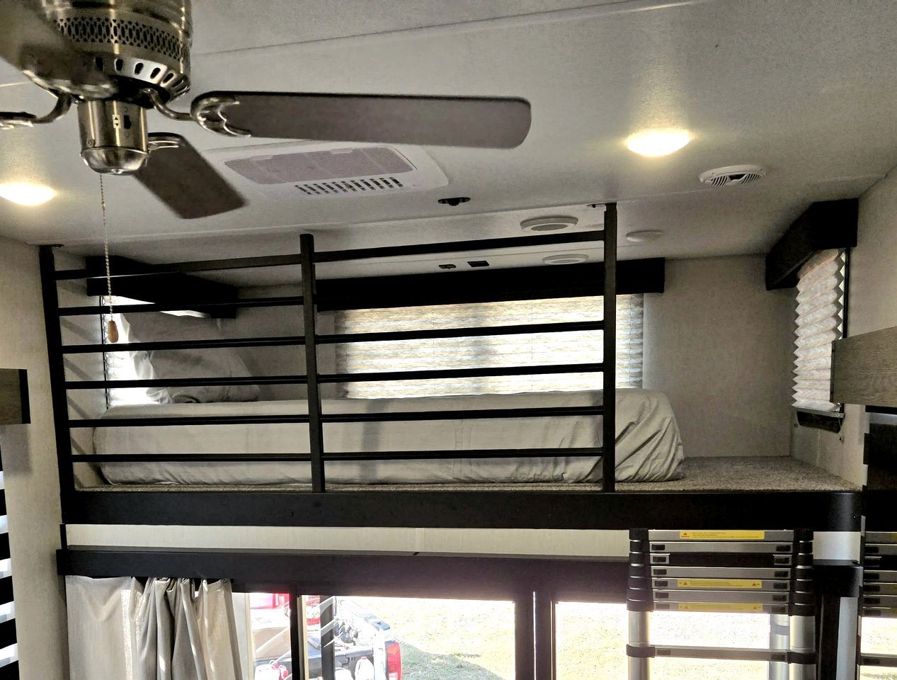 A bunk bed room with a ceiling fan, a window with curtains, and a view of the outside.