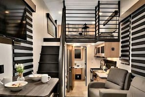 A compact, modern interior with a kitchen, dining area, and seating space, featuring a mezzanine level and a staircase. - Modern Lofted Tiny House Fully Equipped with Lake Views in Texas (Quitman)