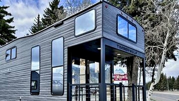 A modern RV with a covered front area, large windows, and a ramp for access.