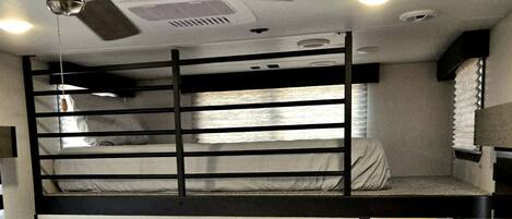 Habitación con literas, ventilador de techo, ventana con cortinas y vistas al exterior.