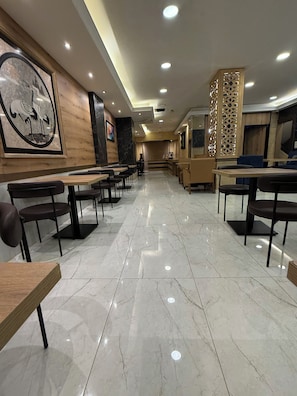 A spacious restaurant with marble flooring, wooden tables, and chairs, featuring a large wall-mounted painting and a decorative partition. - Weekend Hotel (Beirut)
