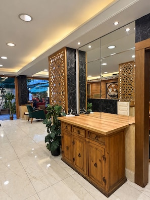 A reception area with a wooden reception desk, a large mirror, and a seating area with green chairs. - Weekend Hotel (Beirut)