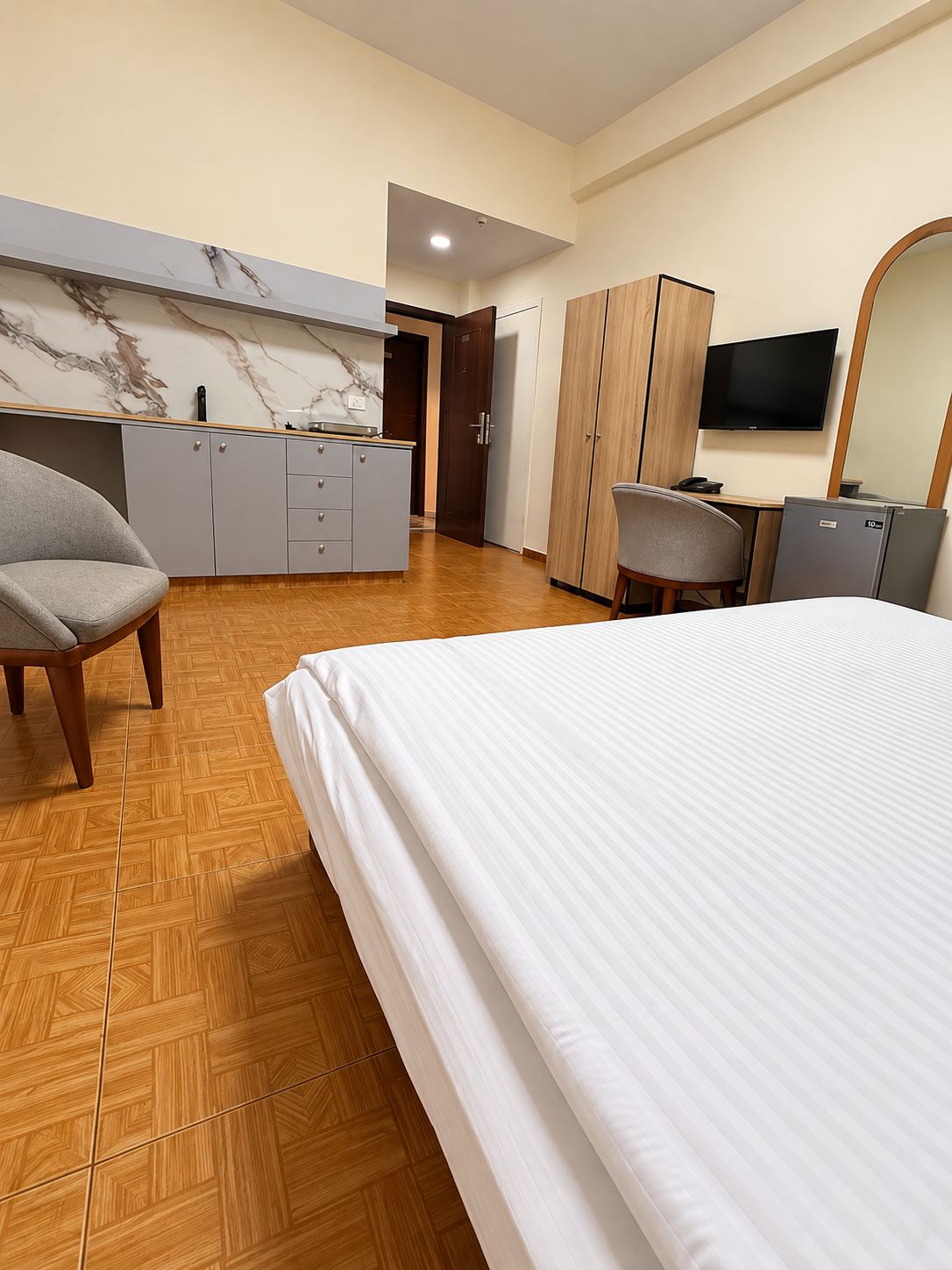 A hotel room with a bed, a desk, a chair, a wardrobe, and a television.