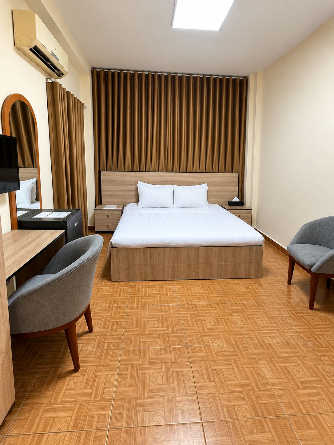 A hotel room with a large bed, a desk with a chair, a TV, and a window with curtains.