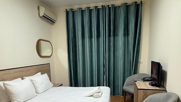 A hotel room with a bed, a desk with a computer, a chair, a TV, an air conditioner, and a window with curtains. - Weekend Hotel (Beirut)