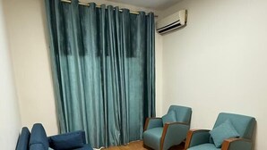 A living room with a sofa, two armchairs, a large window with curtains, and an air conditioning unit. - Weekend Hotel (Beirut)