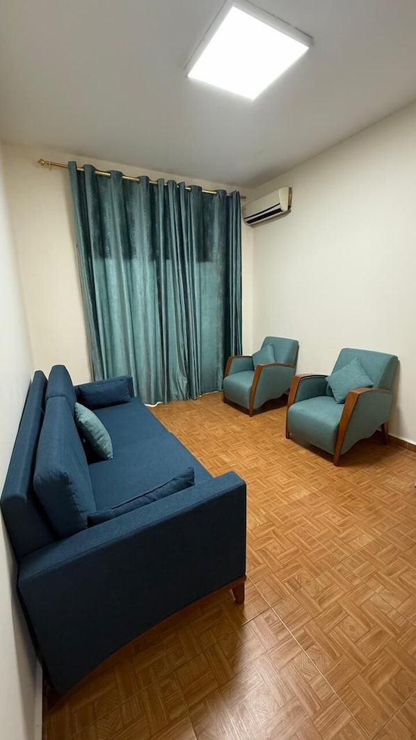 A living room with a sofa, two armchairs, a large window with curtains, and an air conditioning unit. - Weekend Hotel (Beirut)