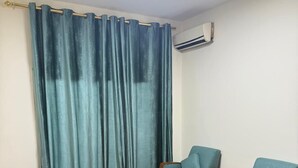 A room with a sofa, two armchairs, a patterned curtain, a ceiling light, and an air conditioning unit. - Weekend Hotel (Beirut)