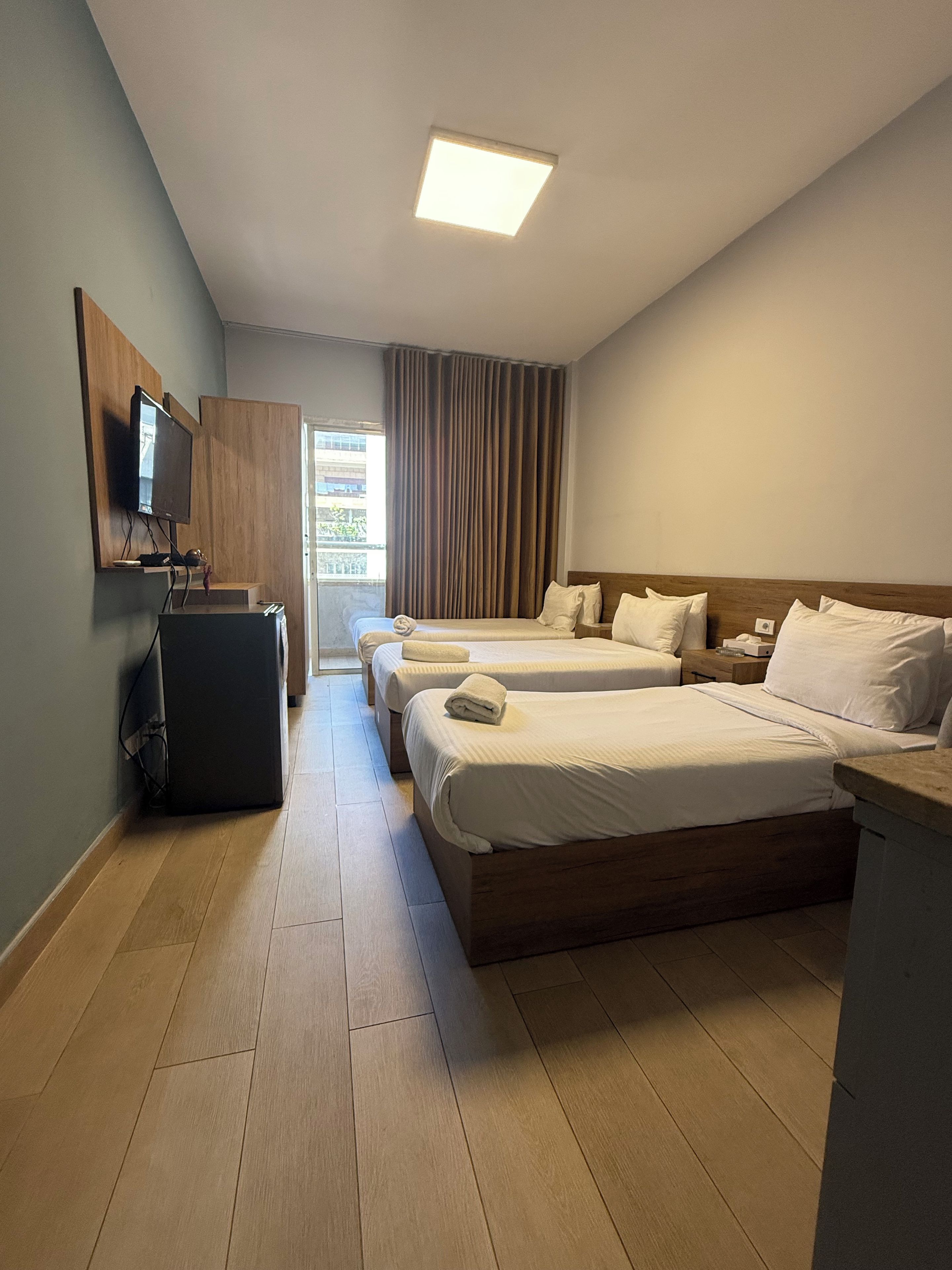 Een hotelkamer met twee bedden, een flatscreen televisie, een bureau en een raam met gordijnen.