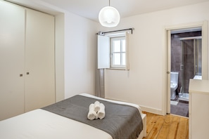 A bedroom with a bed, a bedside table, a mirror, and a door leading to a bathroom.