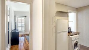 A compact kitchen with a washing machine, a refrigerator, and a window with curtains. - Bairro Alto Typical by Homing (Lisbon)