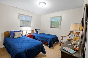A bedroom with two beds, a nightstand, a lamp, a chair, and a small table with a lamp and decorative items.