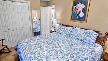 A bedroom with a bed, a rocking chair, a bedside table, a lamp, and a framed picture on the wall.