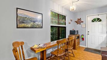 A dining area with a wooden table and chairs, a framed landscape picture, a window with blinds, and a white door.