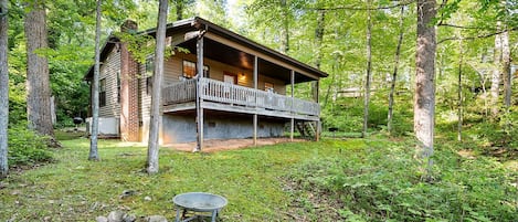 A cabin with a porch, surrounded by trees and a fire pit.
