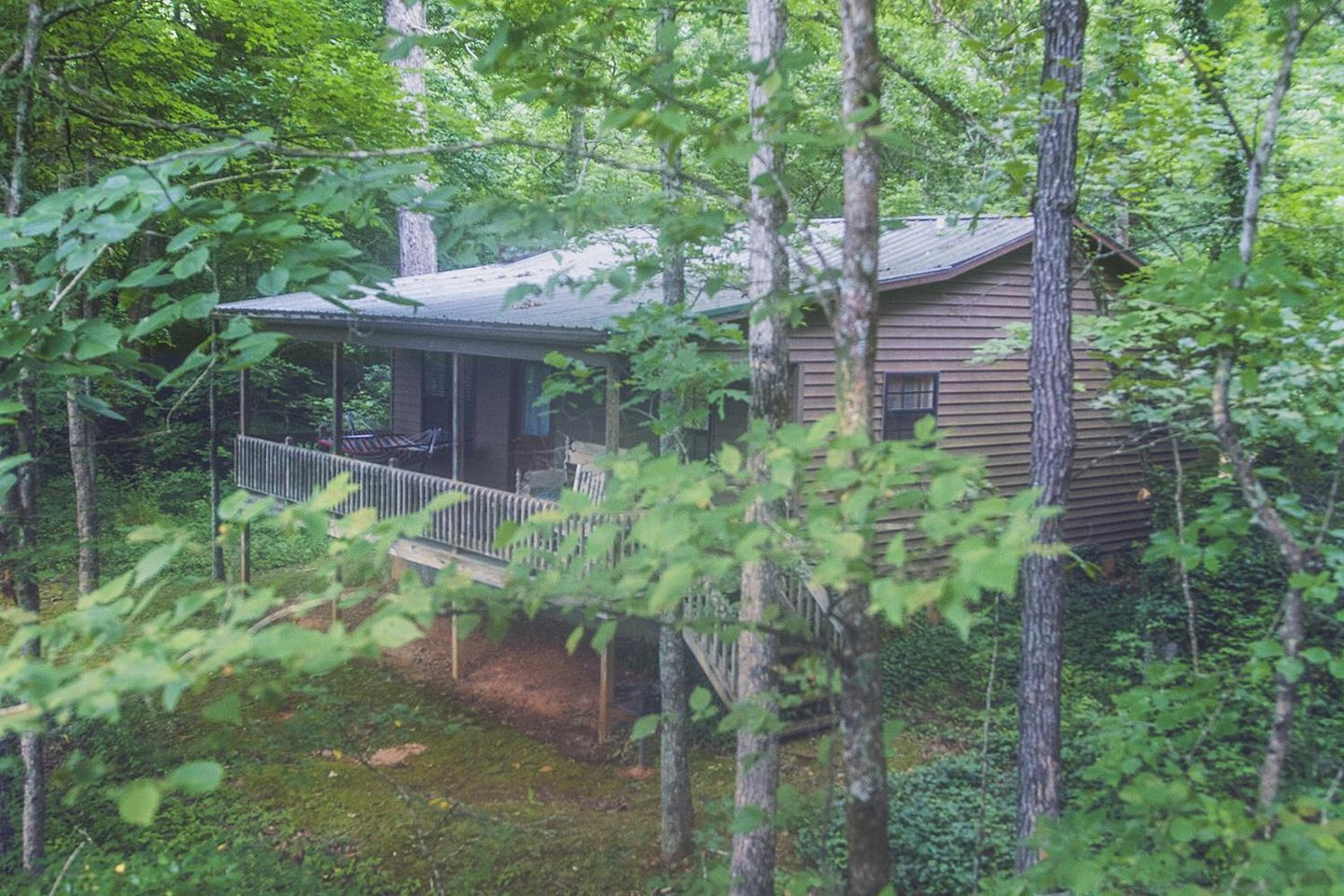 Une cabane entourée d’arbres, dotée d’un porche et d’une terrasse couverte.