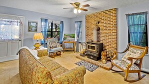A living room with a fireplace, a ceiling fan, and a brick wall.