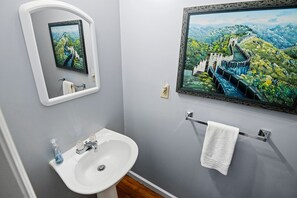 Casa de banho com lavatório, espelho, porta-toalhas e um quadro com uma paisagem.