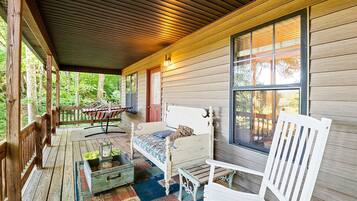 A wooden cabin with a porch, a bed, a bench, and a hammock.