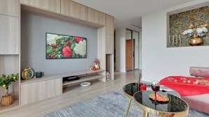 A modern living room with a flat-screen TV mounted on a wooden wall, a glass coffee table, a red sofa, and a stone wall decoration.