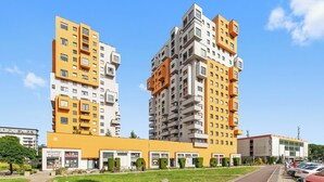 Two high-rise apartment buildings with balconies, a commercial building in the foreground, and a parking area.