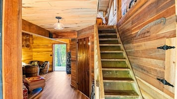 A wooden interior with a staircase, a door leading outside, and a hanging light fixture.