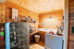 A cozy cabin-style kitchen with wooden walls, a chalkboard fridge, and a sink.
