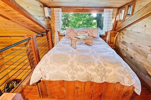 Una habitación de cabaña de madera con una cama, una mesita y una ventana con cortinas.