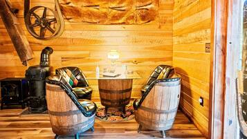 A wooden interior with two leather chairs, a table, a lamp, and a wood-burning stove.