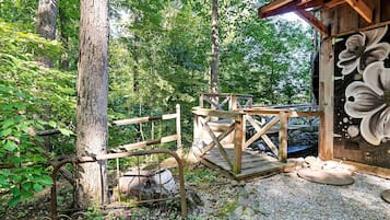 A rustic wooden deck with a metal railing, surrounded by trees and a gravel path.