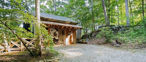 A rustic wooden cabin with a gravel path leading to it, surrounded by dense forest.