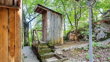 A rustic wooden structure with a staircase leading to a door, surrounded by trees and a stone path.