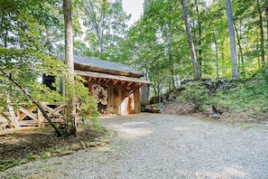 A rustic wooden cabin with a gravel path leading to it, surrounded by dense forest.