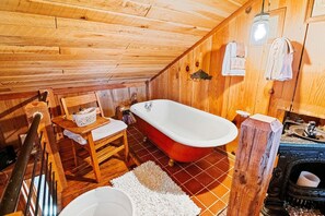 A wooden cabin bathroom with a red bathtub, wooden walls, a white sink, and a rustic wooden chair. - Luxury Cabin for Two with Beautiful River Views near Knoxville (Greeneville)