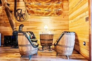 A rustic interior with wooden walls, a large fur rug, a wooden barrel-shaped table, and a vintage stove.