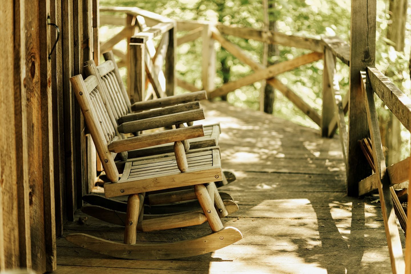 A wooden rocking chair on a porch with a wooden railing.
