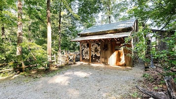 A rustic wooden cabin with a gravel path leading to it, surrounded by dense forest.