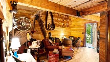 A rustic wooden interior with a dining area, leather chairs, a table with a lamp, and a large wheel.