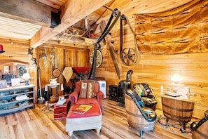 A rustic wooden cabin interior with a red armchair, a wooden table, a vintage stove, and various wooden walls and ceilings.