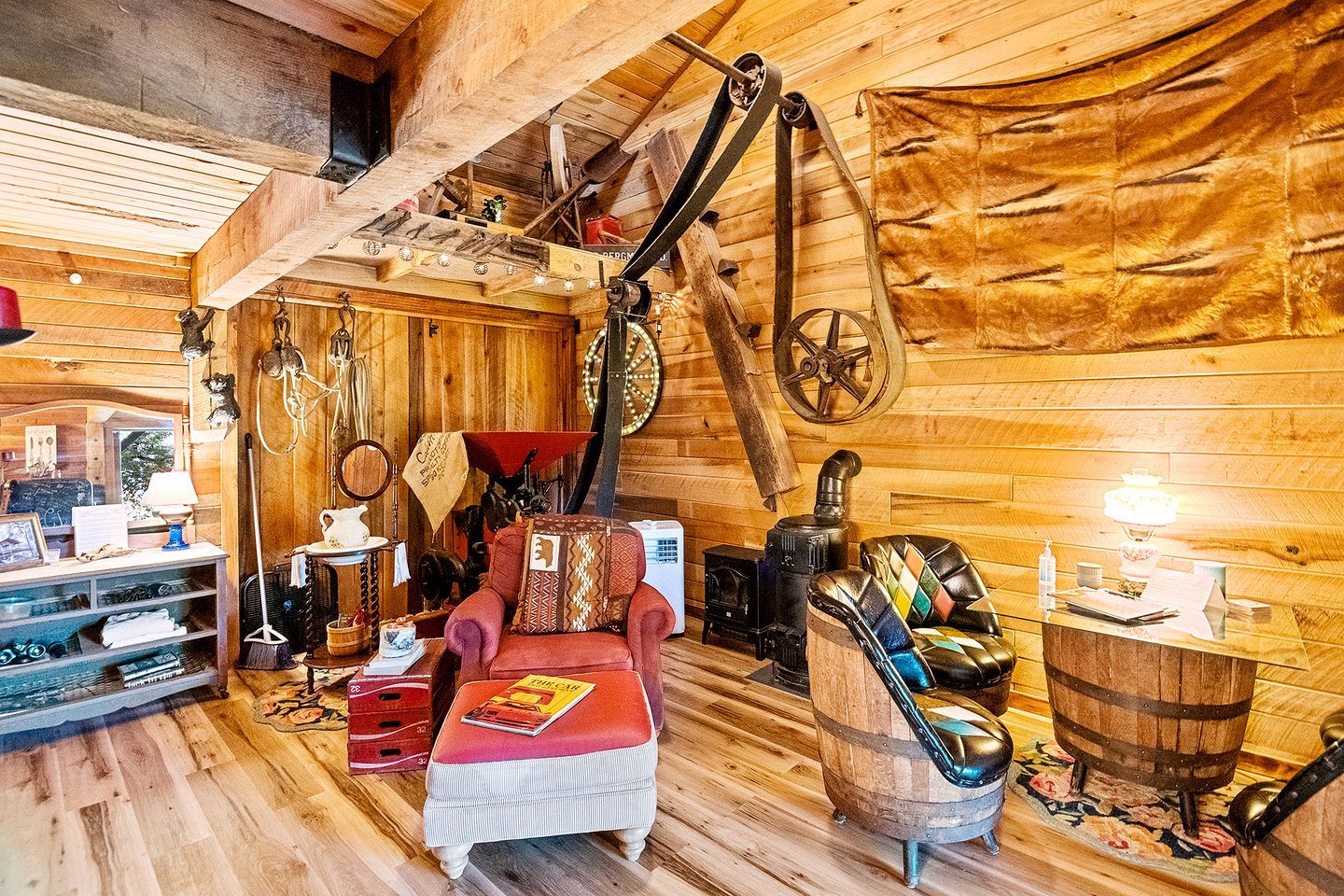 A rustic wooden cabin interior with a red armchair, a wooden table, a vintage stove, and various wooden walls and ceilings.