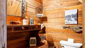 A wooden cabin-style bathroom with a toilet, sink, and mirror.