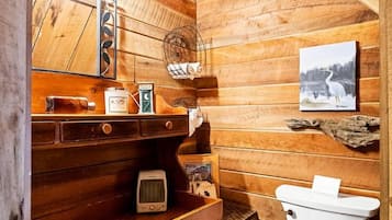 Casa de banho em estilo cabana de madeira, com sanita, lavatório e espelho.