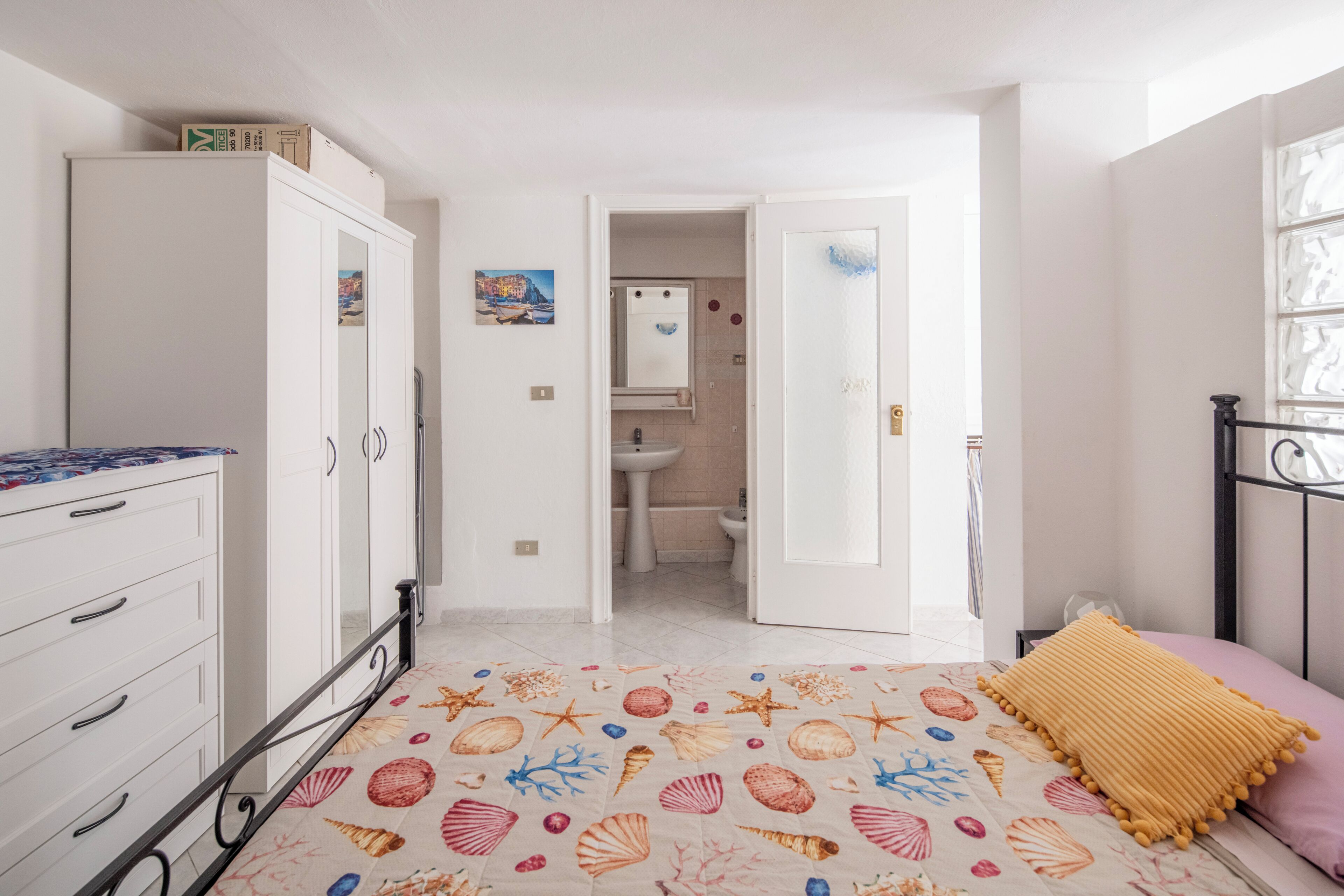 A bedroom with a bed, a wardrobe, a bathroom with a sink and mirror, and a hallway leading to another room.