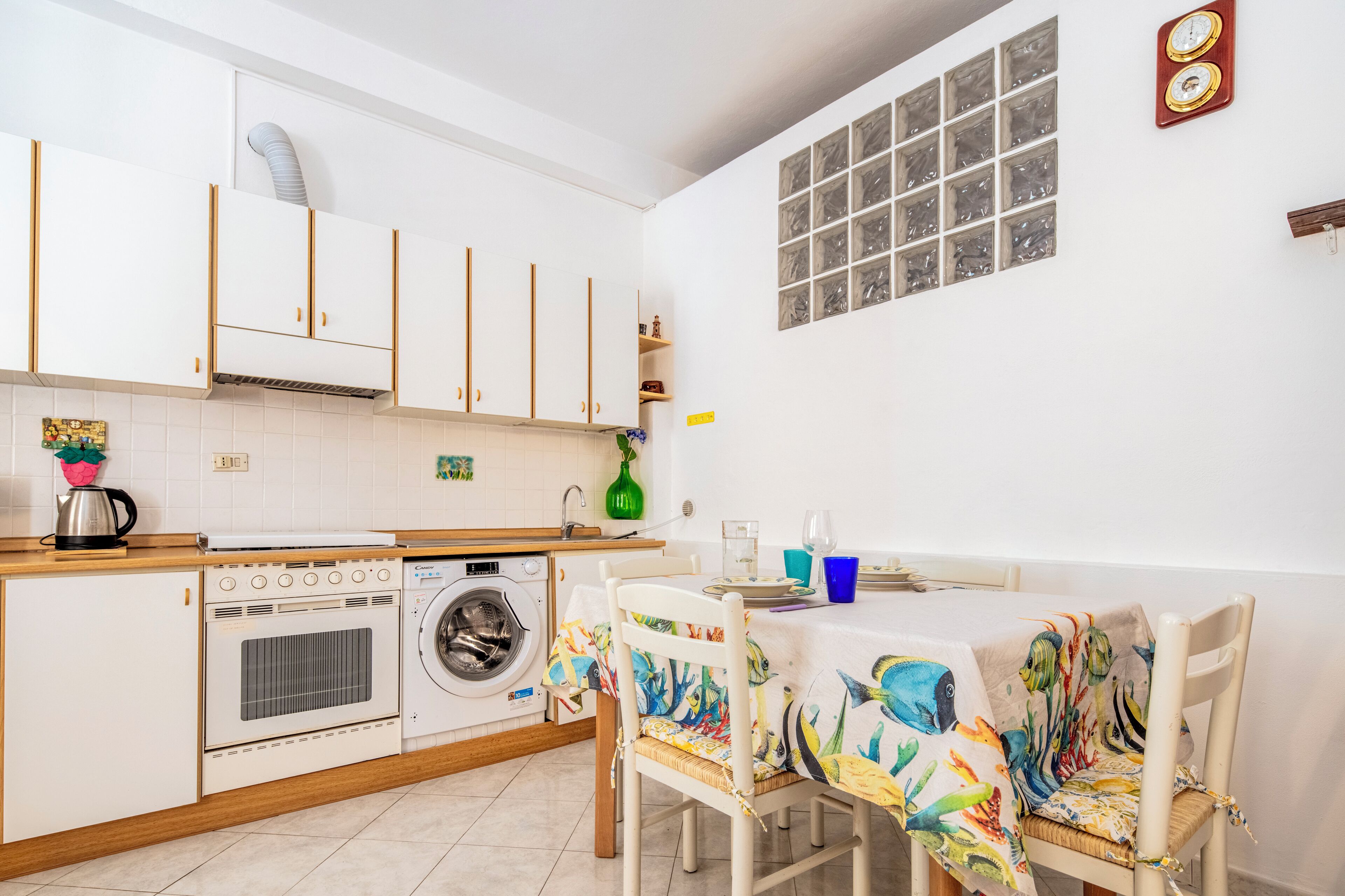A compact kitchen with white cabinets, a washing machine, a coffee maker, and a dining area with a table and chairs.