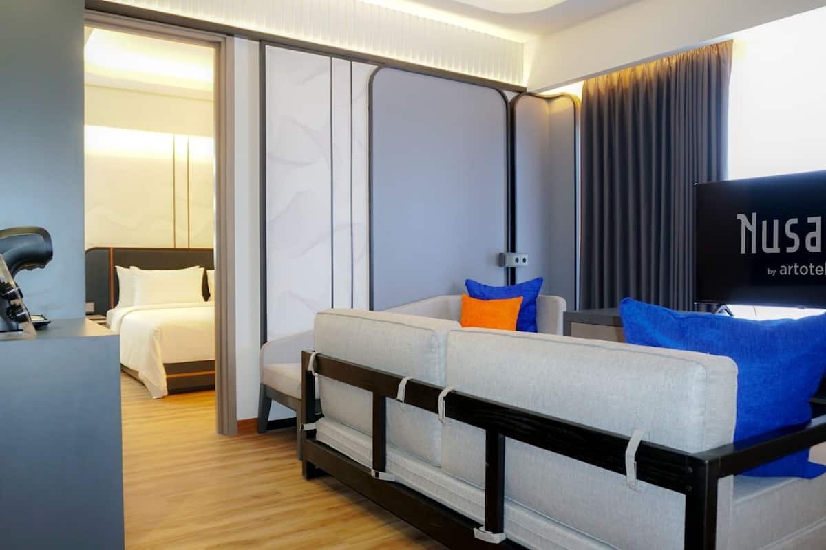 A modern hotel room with a sofa, a bed, a desk with a lamp, and a television.