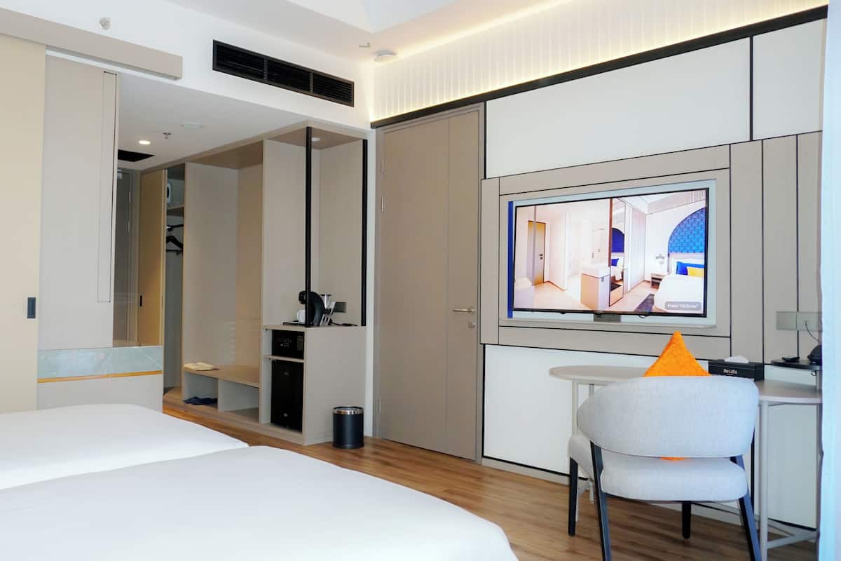 A modern hotel room with a bed, a desk, a chair, and a TV displaying a room layout.